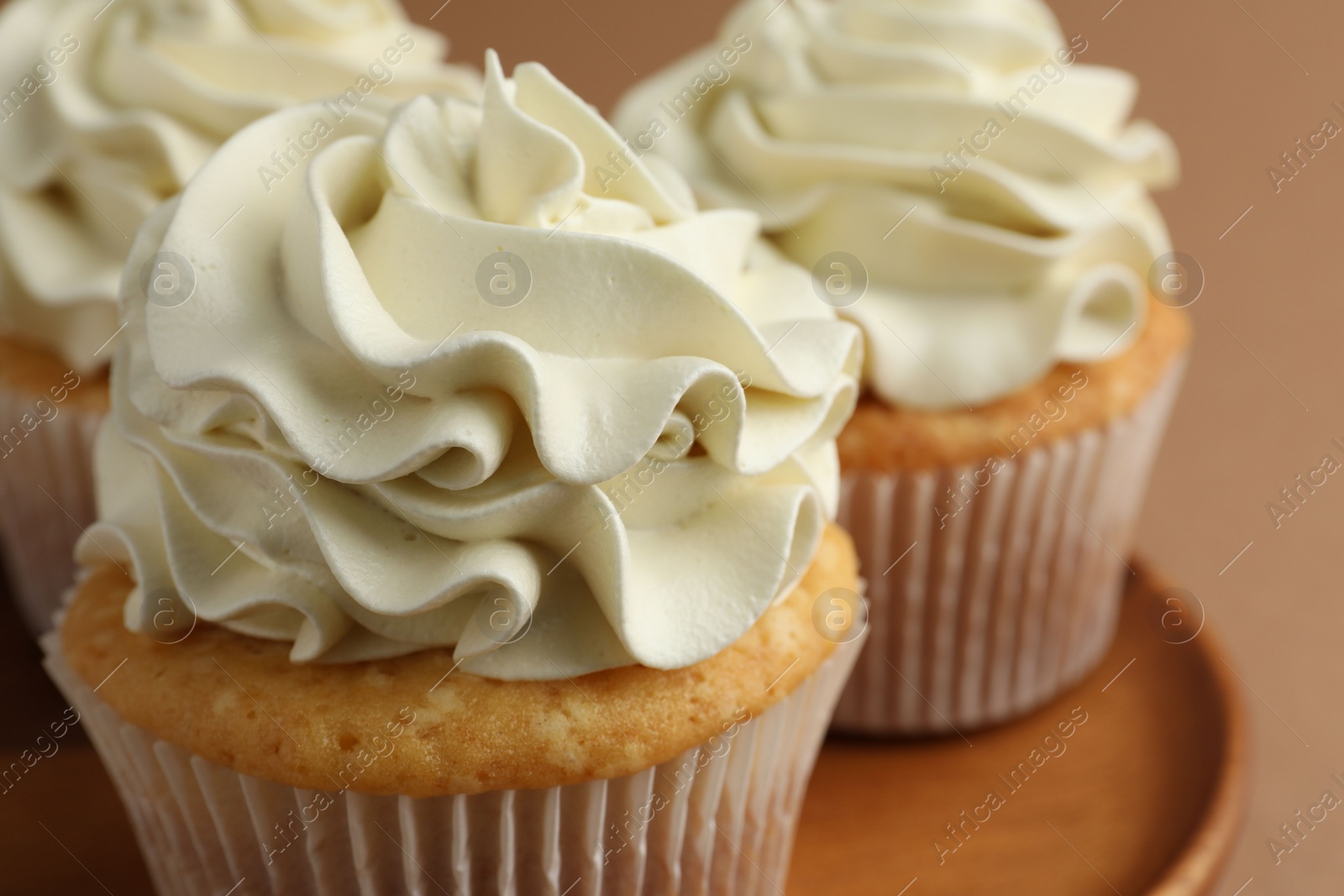 Photo of Tasty vanilla cupcakes with cream on dark beige background, closeup