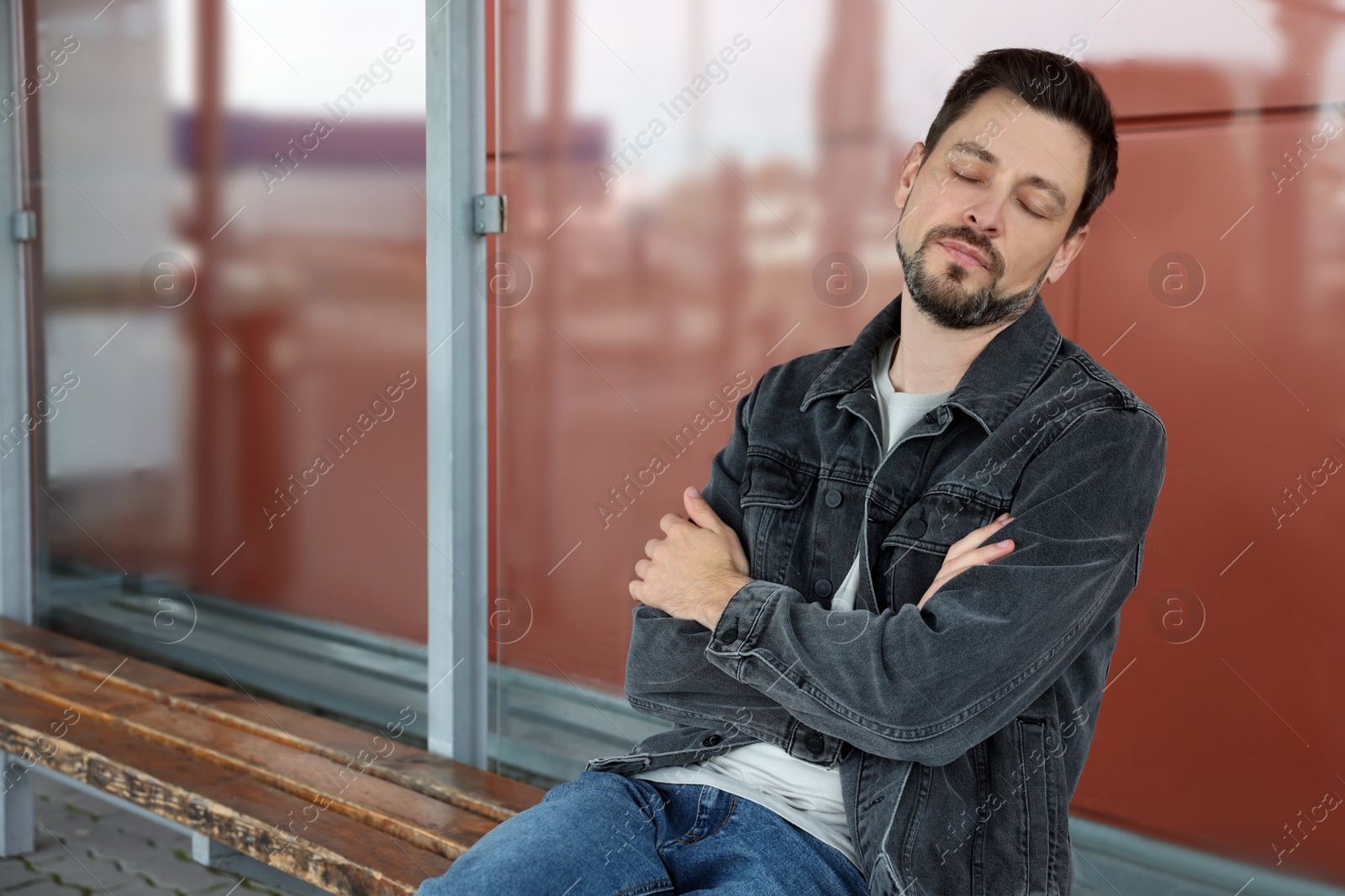 Photo of Tired man sleeping at public transport stop outdoors