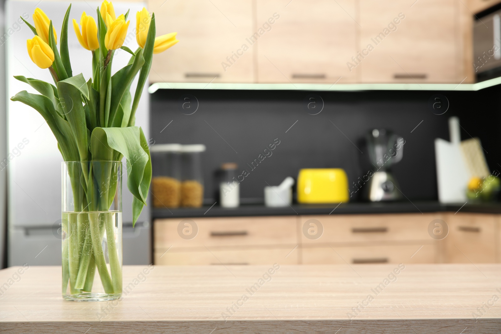 Photo of Glass vase with tulips on table in kitchen