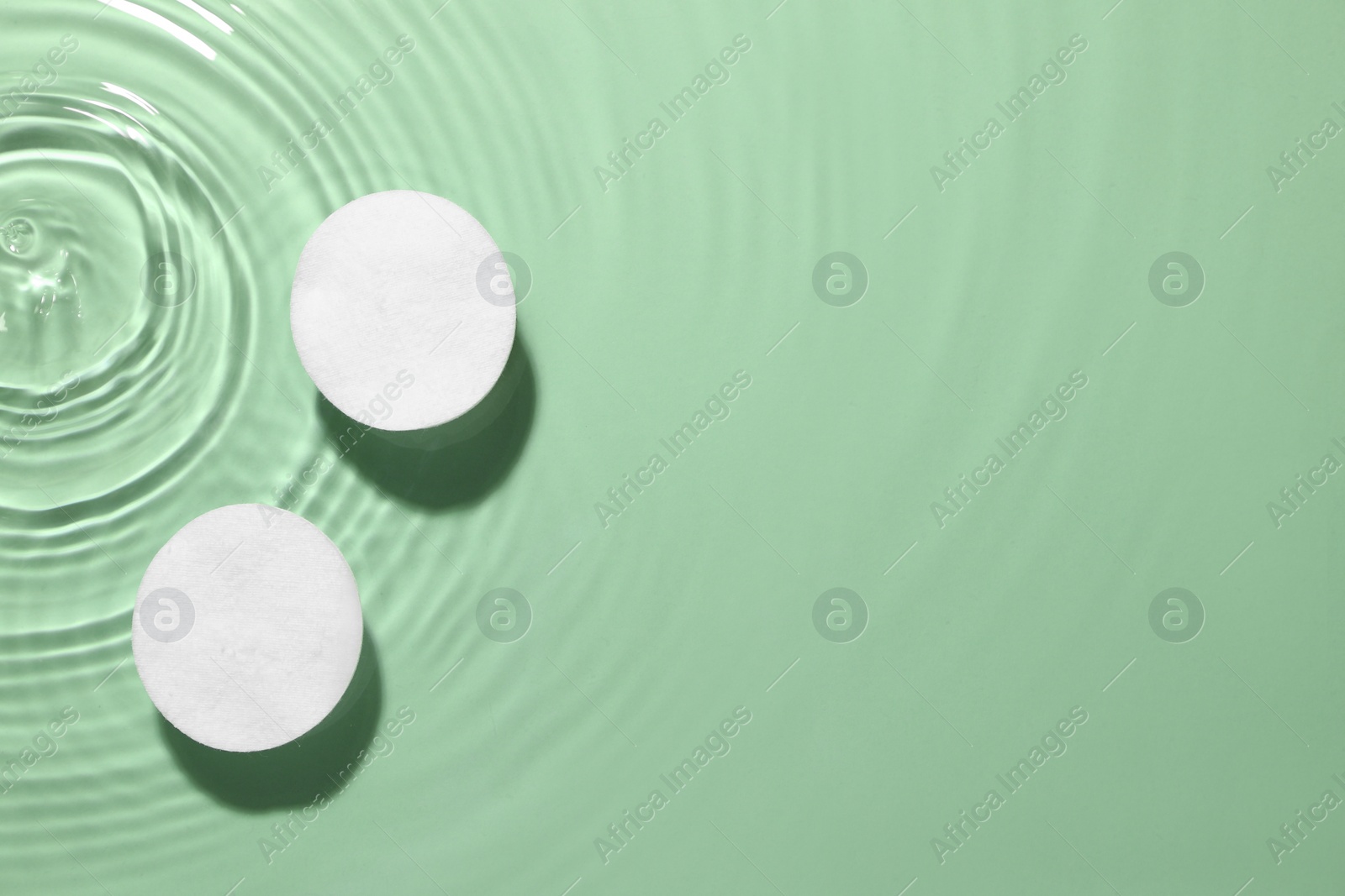 Image of Cotton pads in micellar water on green background, top view. Space for text