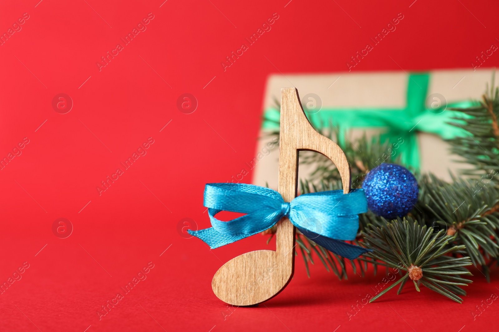 Photo of Wooden music note with blue bow and fir tree branches on red background, space for text. Christmas celebration