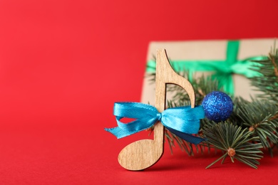 Photo of Wooden music note with blue bow and fir tree branches on red background, space for text. Christmas celebration