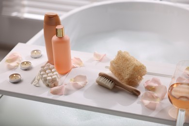 Photo of Wooden tray with toiletries and flower petals on bathtub in bathroom