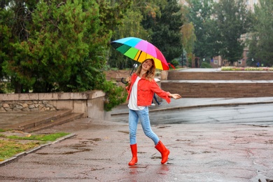 Photo of Happy young woman with bright umbrella under rain outdoors