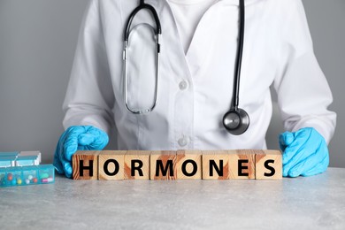 Photo of Doctor near word HORMONES made with wooden cubes at grey table, closeup