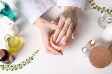 Photo of Dermatologist with jar testing cosmetic product at white table, top view