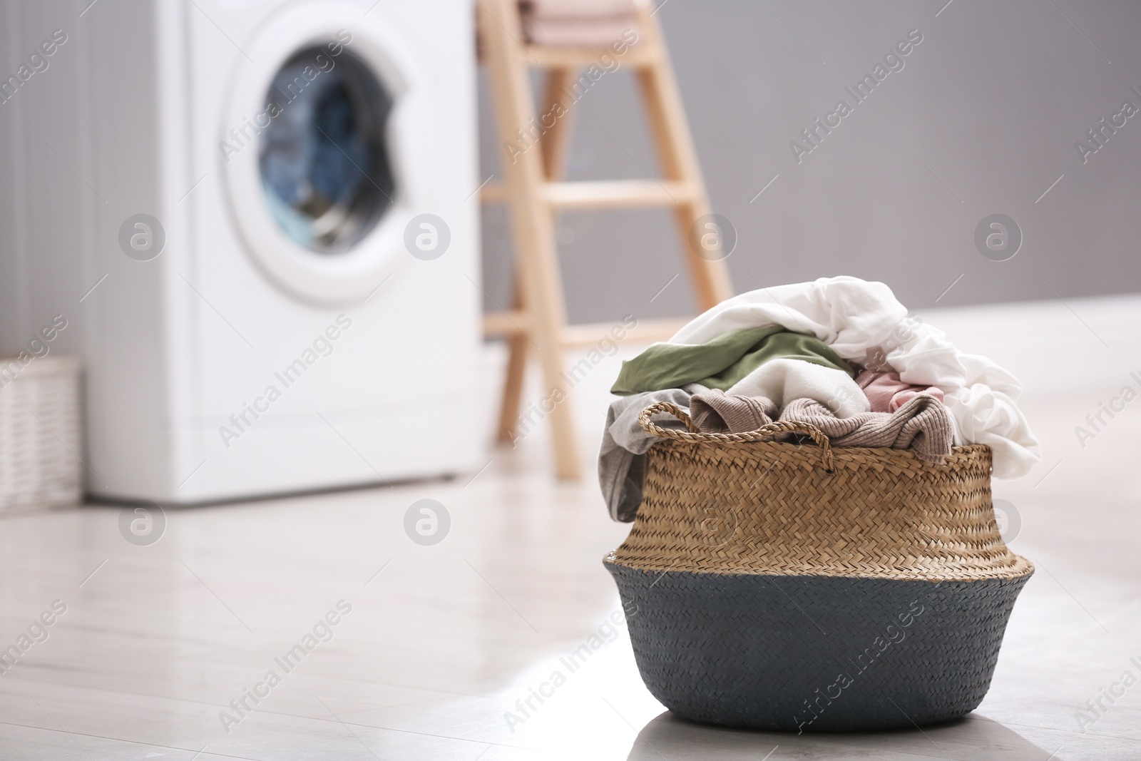 Photo of Wicker basket with dirty laundry on floor indoors, space for text