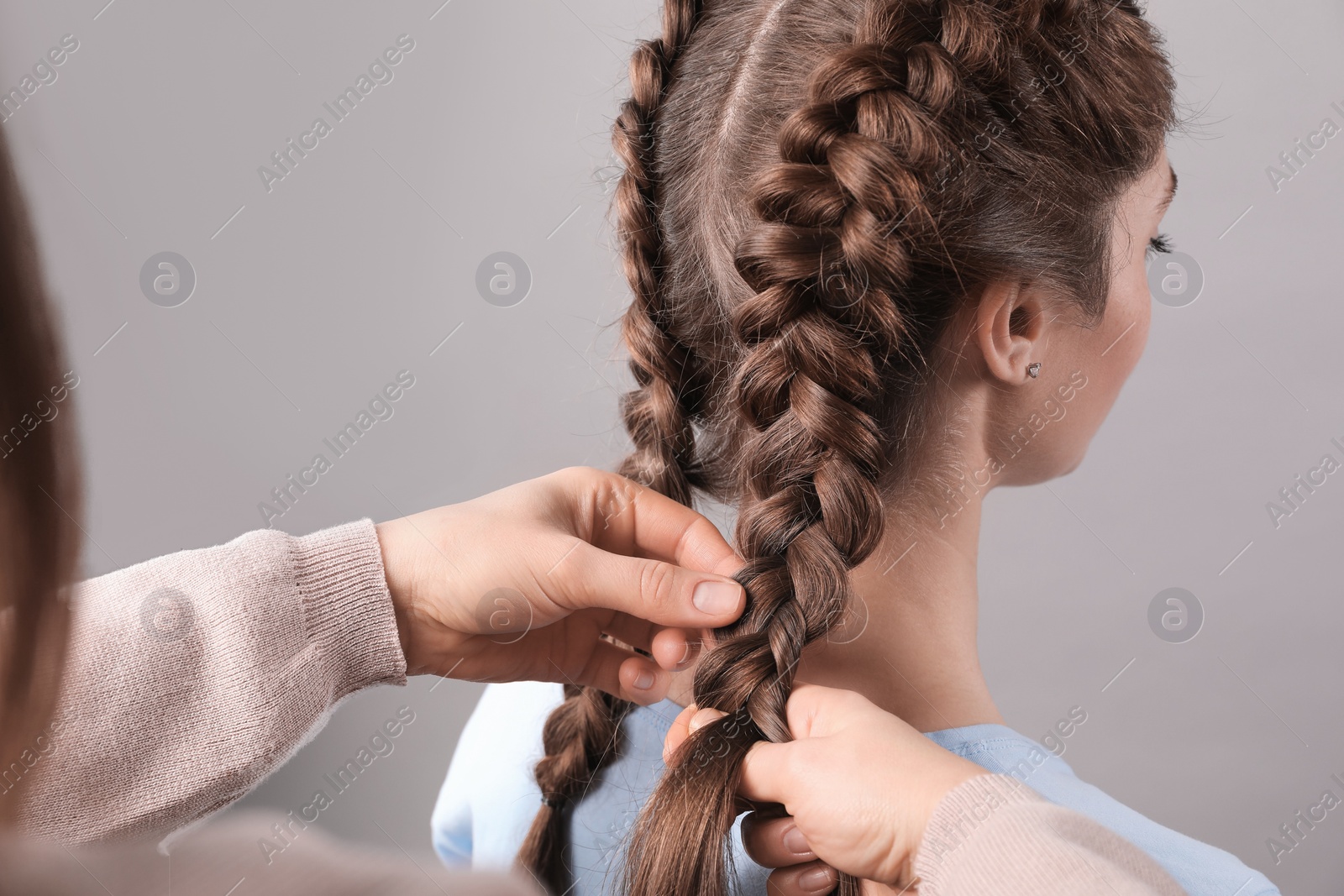 Photo of Professional stylist braiding woman's hair on grey background, closeup