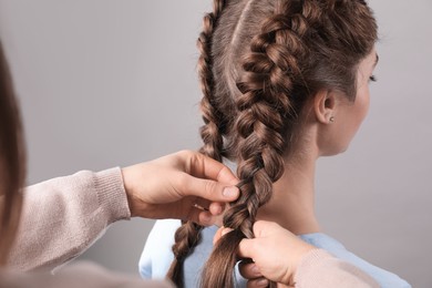 Photo of Professional stylist braiding woman's hair on grey background, closeup