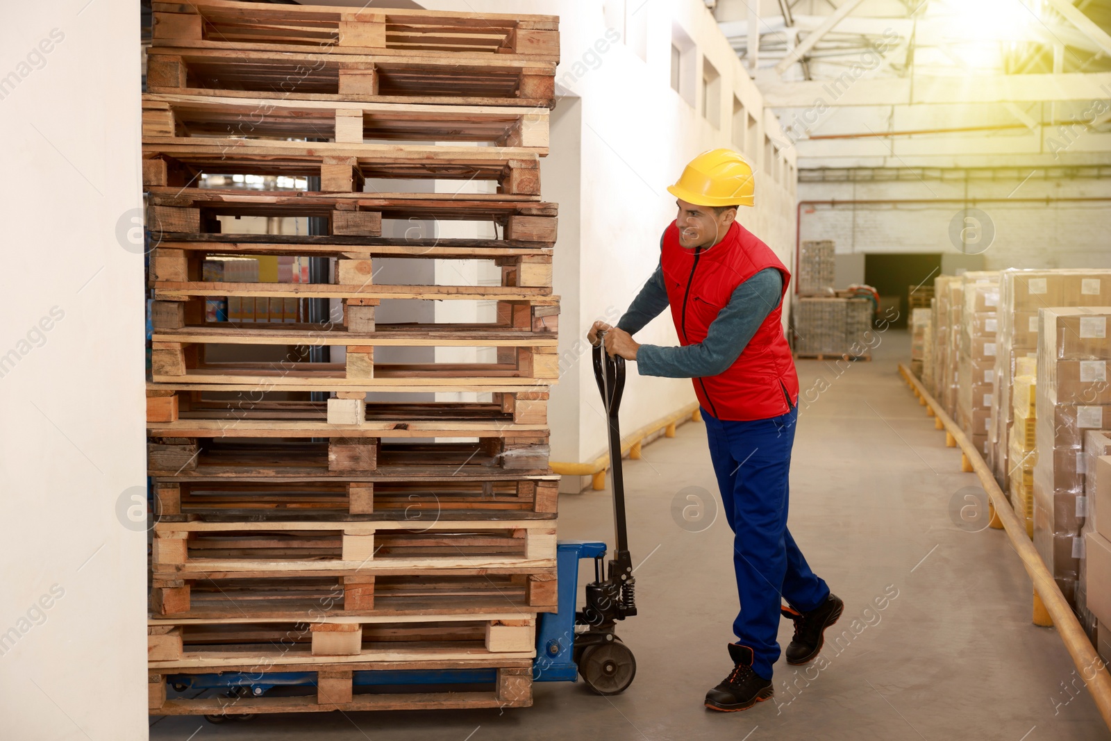 Image of Worker moving wooden pallets with manual forklift in warehouse