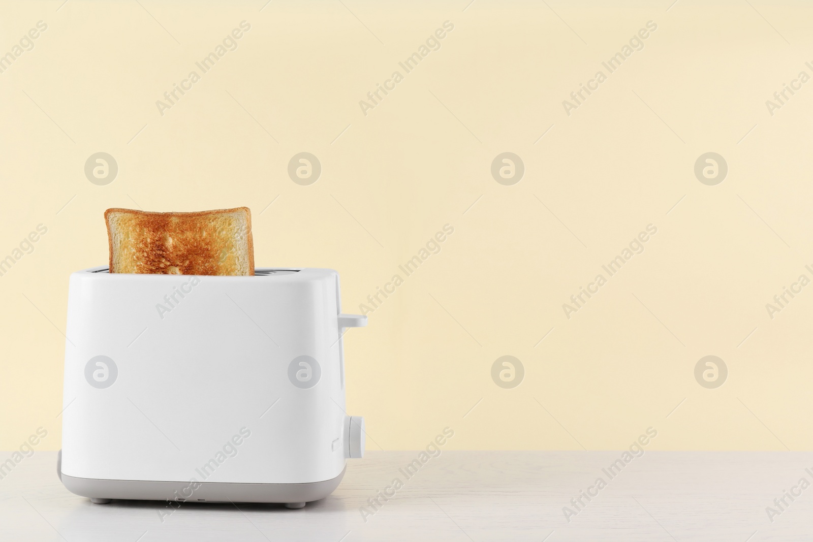 Photo of Modern toaster with slice of bread on white wooden table. Space for text