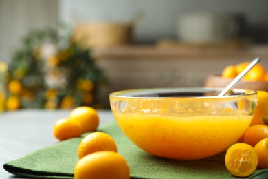 Delicious kumquat jam in bowl and fresh fruits on table, closeup. Space for text