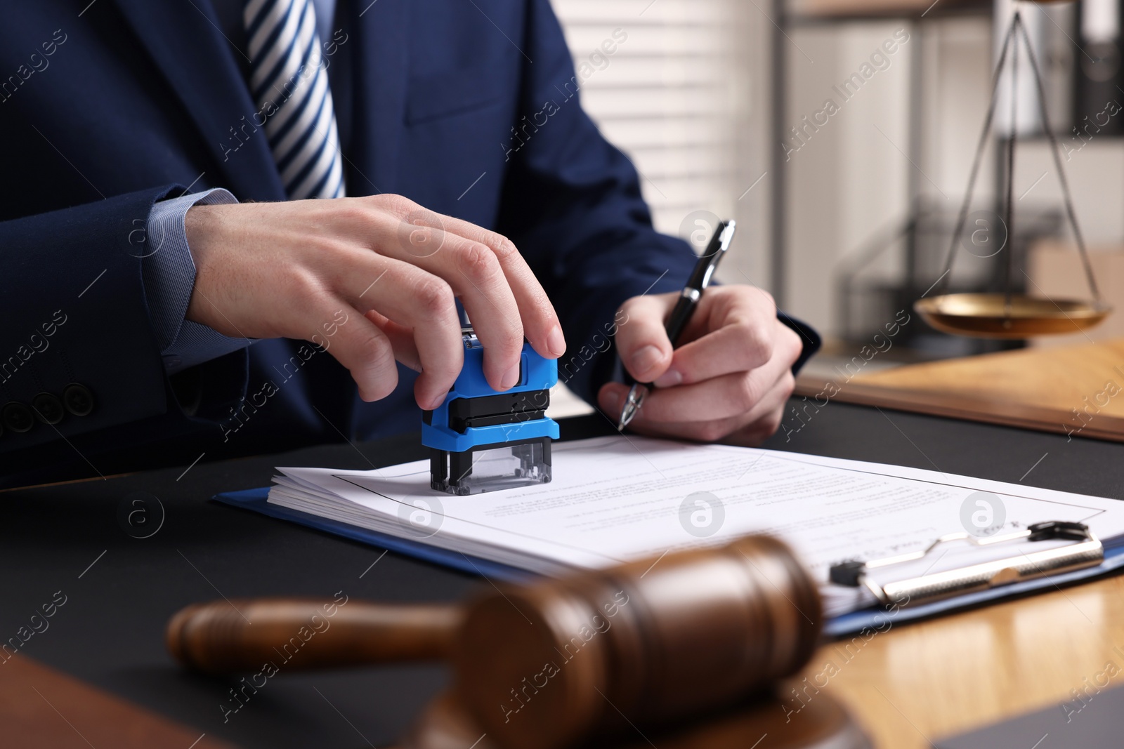 Photo of Notary with pen stamping document at table in office, closeup