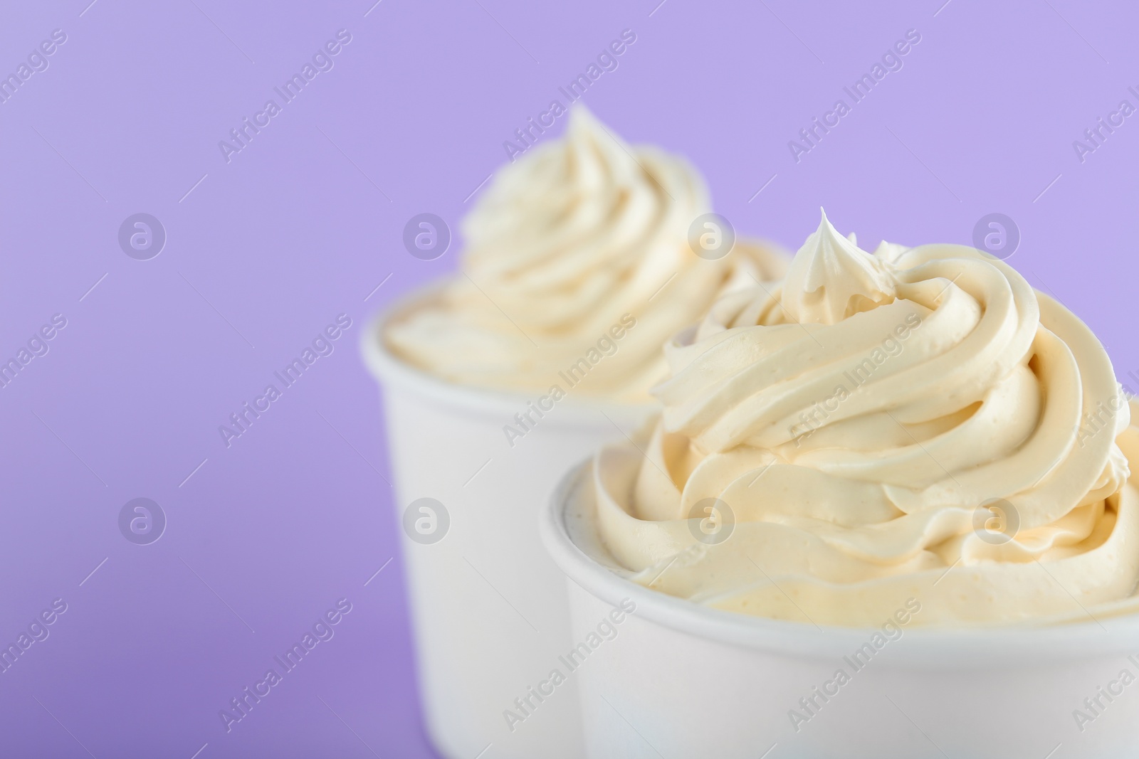 Photo of Cups with tasty frozen yogurt on violet background, closeup. Space for text