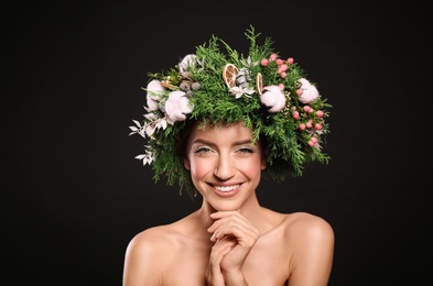 Happy young woman wearing wreath on black background