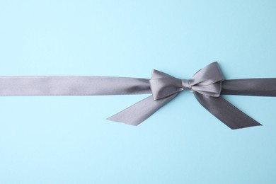 Photo of Grey satin ribbon with bow on light blue background, top view