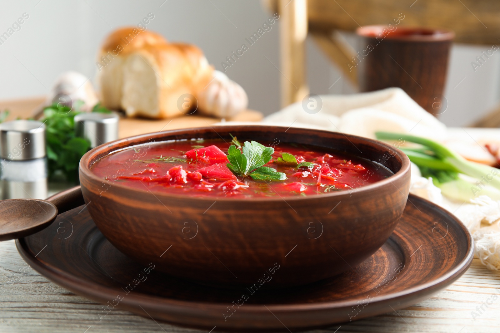 Photo of Stylish brown clay bowl with Ukrainian borsch served on white wooden table