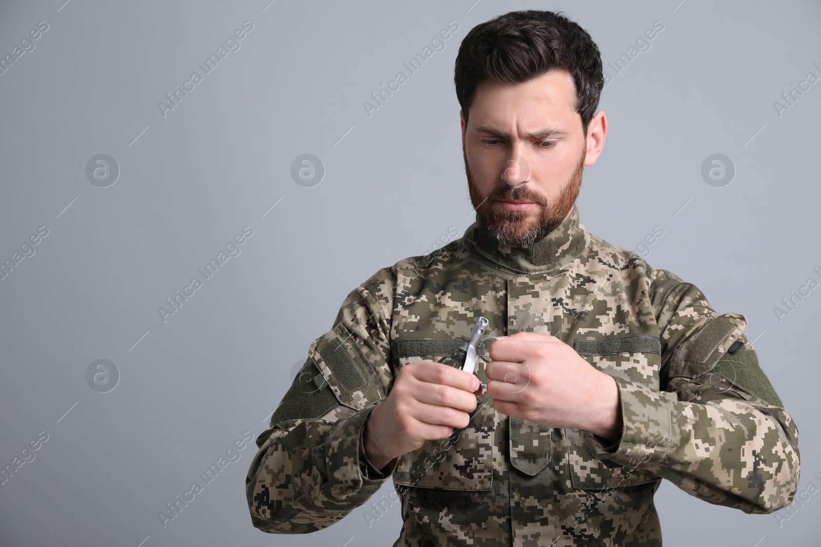 Photo of Soldier pulling safety pin out of hand grenade on light grey background. Military service