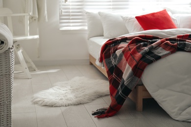 Comfortable bed with warm checkered plaid in stylish room interior