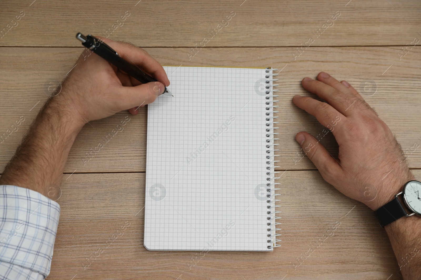 Photo of Left-handed man writing in notebook at wooden table, top view