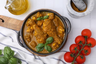 Delicious chicken with curry sauce and ingredients served on white tiled table, flat lay