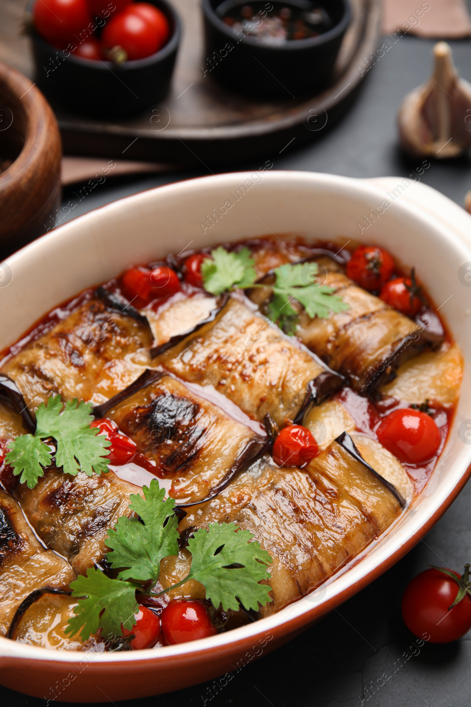 Photo of Tasty eggplant rolls with tomatoes, cheese and parsley in baking dish on black table, closeup