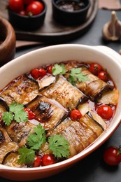 Tasty eggplant rolls with tomatoes, cheese and parsley in baking dish on black table, closeup