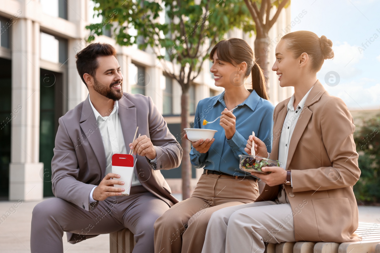 Photo of Business lunch. Happy colleagues spending time together during break on bench outdoors