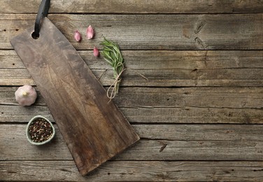 Photo of Cutting board, garlic, pepper and rosemary on wooden table, flat lay. Space for text