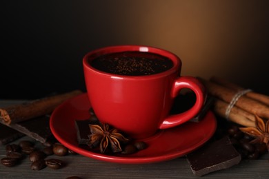 Photo of Cup of delicious hot chocolate, spices and coffee beans on wooden table