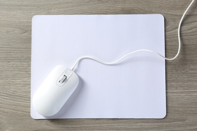 Photo of Wired mouse and mousepad on wooden table, top view