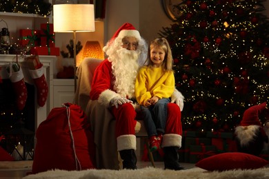 Photo of Merry Christmas. Little girl sitting on Santa's knee at home