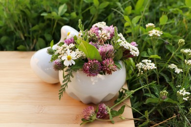 Ceramic mortar with pestle, different wildflowers and herbs on green grass outdoors