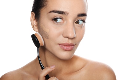 Young woman applying foundation on her face against white background