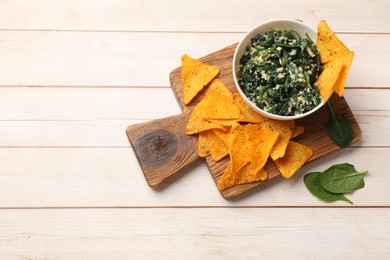 Photo of Tasty spinach dip with eggs in bowl and nachos chips on light wooden table, top view. Space for text