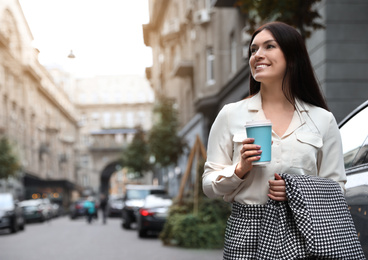 Beautiful woman in stylish suit with cup of coffee on city street