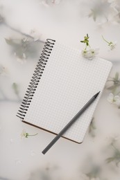 Photo of Guest list. Notebook, pencil and beautiful cherry tree blossoms on spring floral background, flat lay