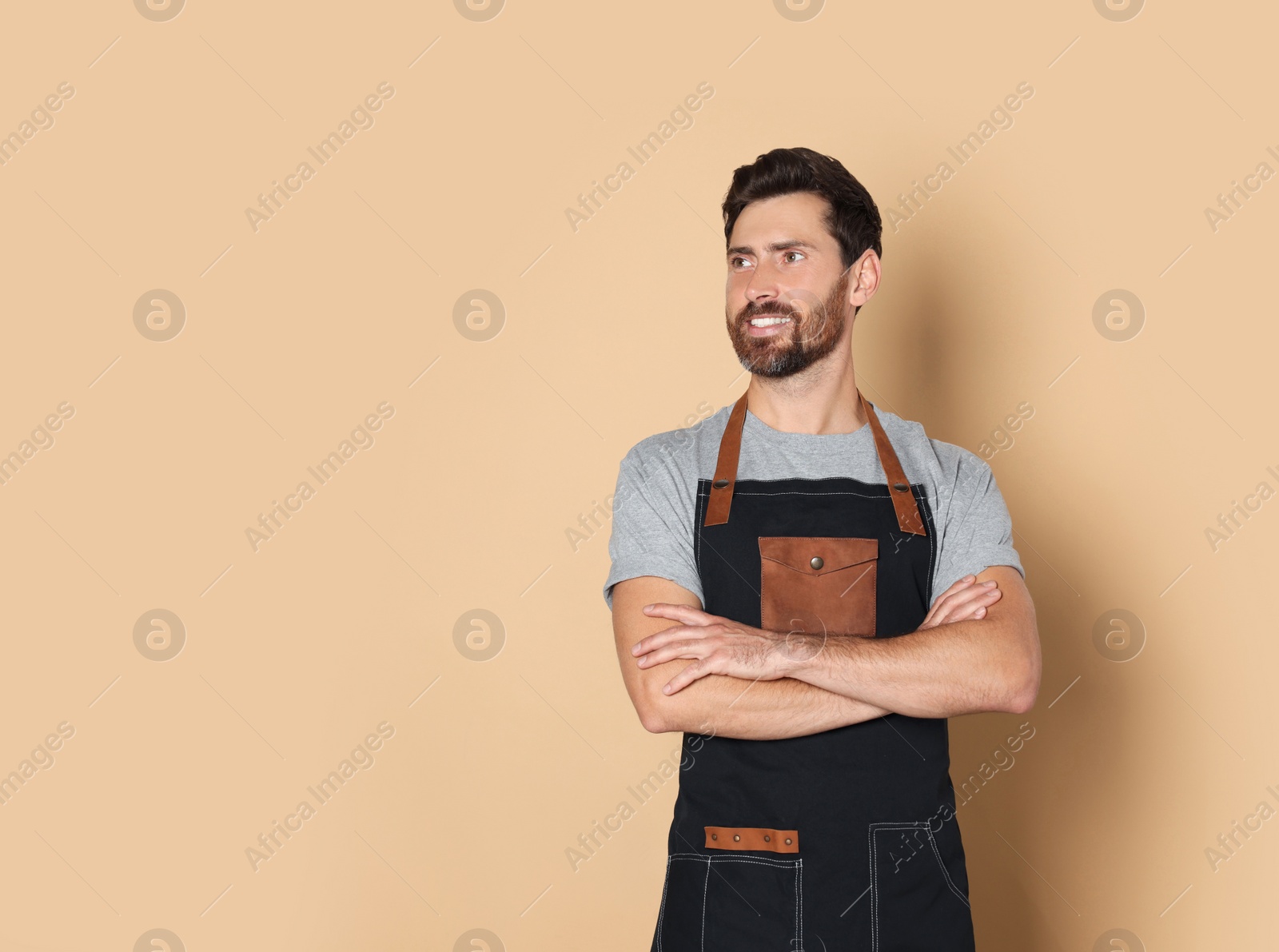 Photo of Smiling hairdresser wearing apron on light brown background, space for text