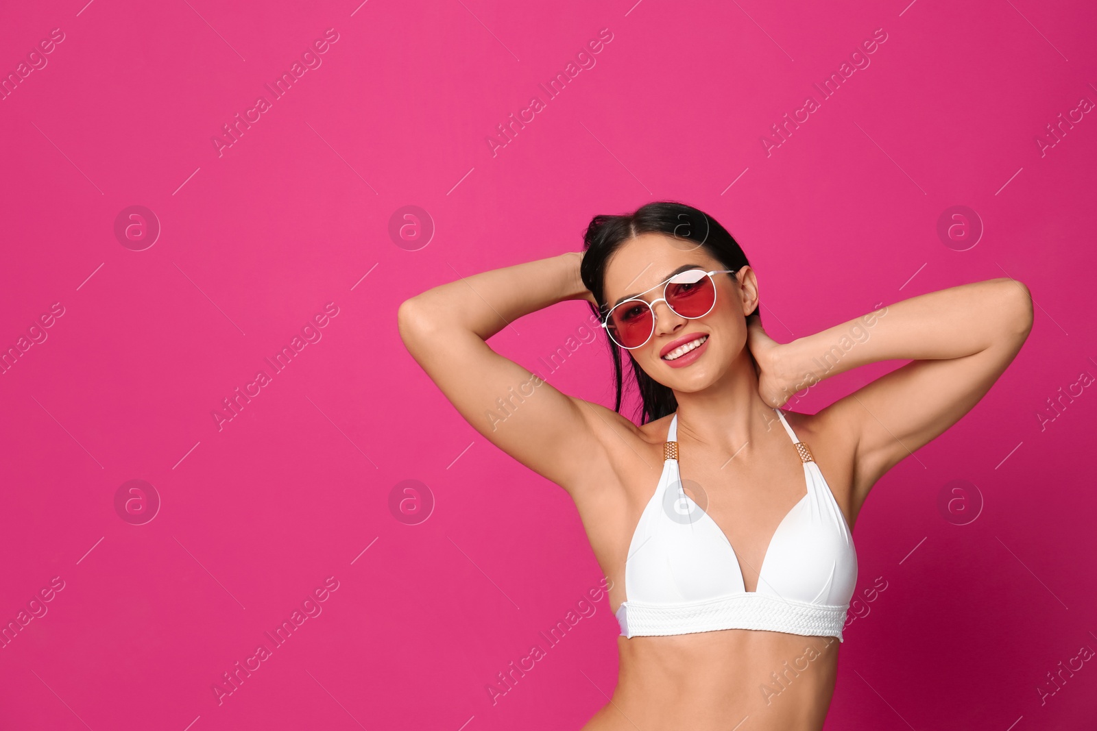 Photo of Beautiful young woman in white bikini with sunglasses on pink background. Space for text