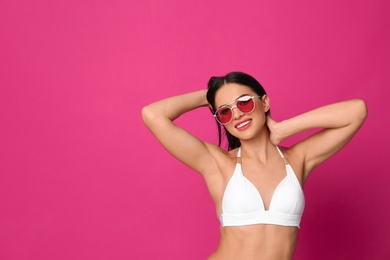 Photo of Beautiful young woman in white bikini with sunglasses on pink background. Space for text