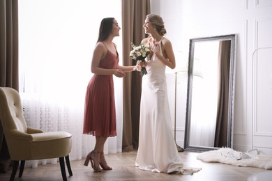 Photo of Gorgeous bride in beautiful wedding dress and her friend near window in room