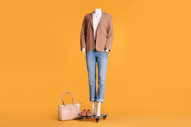 Photo of Female mannequin with accessories dressed in white t-shirt, beige jacket and jeans on orange background. Stylish outfit