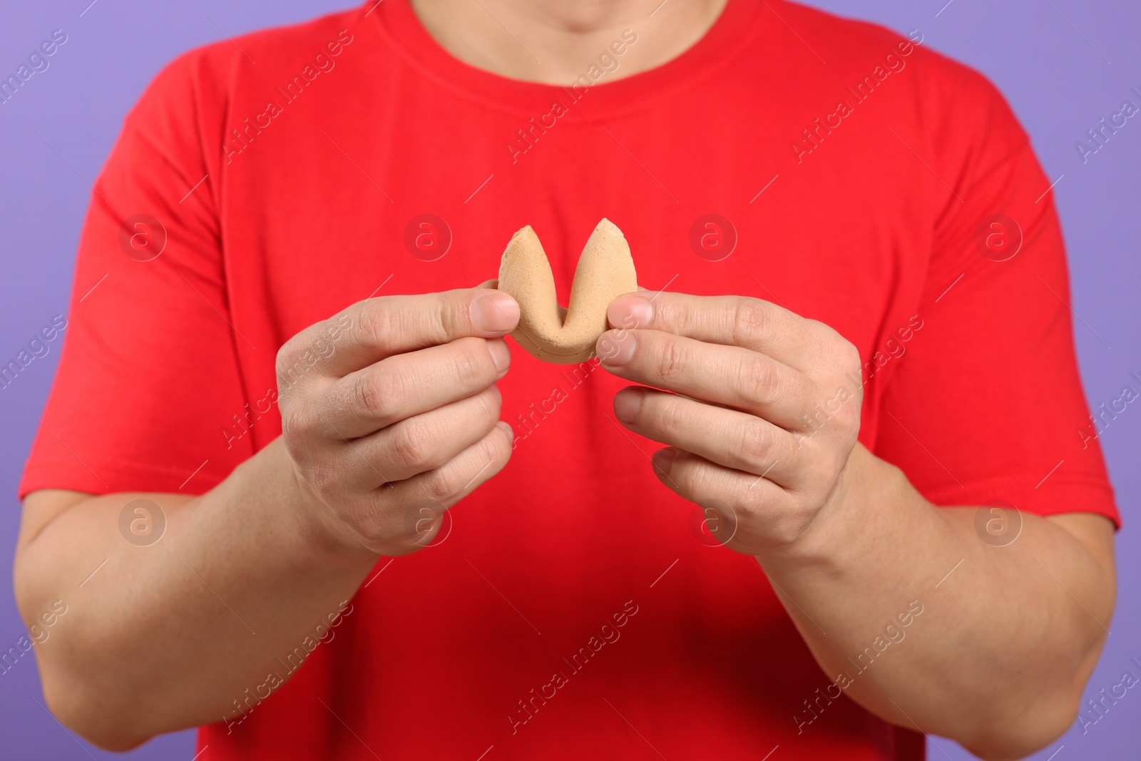 Photo of Man holding tasty fortune cookie with prediction on violet background, closeup