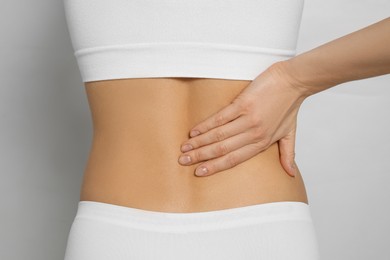 Woman suffering from pain in back on light grey background, closeup