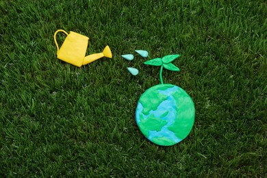 Photo of Happy Earth Day. Flat lay composition with plasticine planet and watering can on green grass