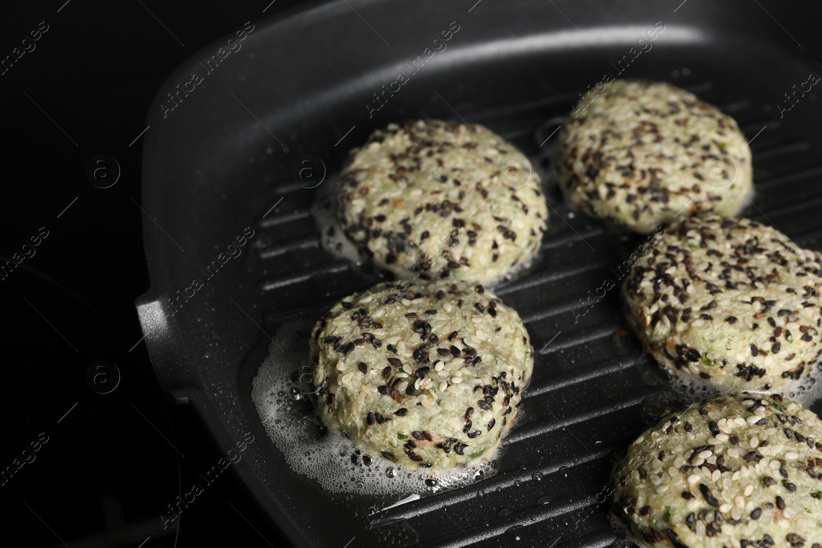 Photo of Cooking tasty vegan cutlets with sesame in grill pan on cooktop, closeup