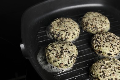 Photo of Cooking tasty vegan cutlets with sesame in grill pan on cooktop, closeup