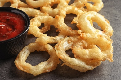 Photo of Delicious golden crispy onion rings and sauce on gray background, closeup