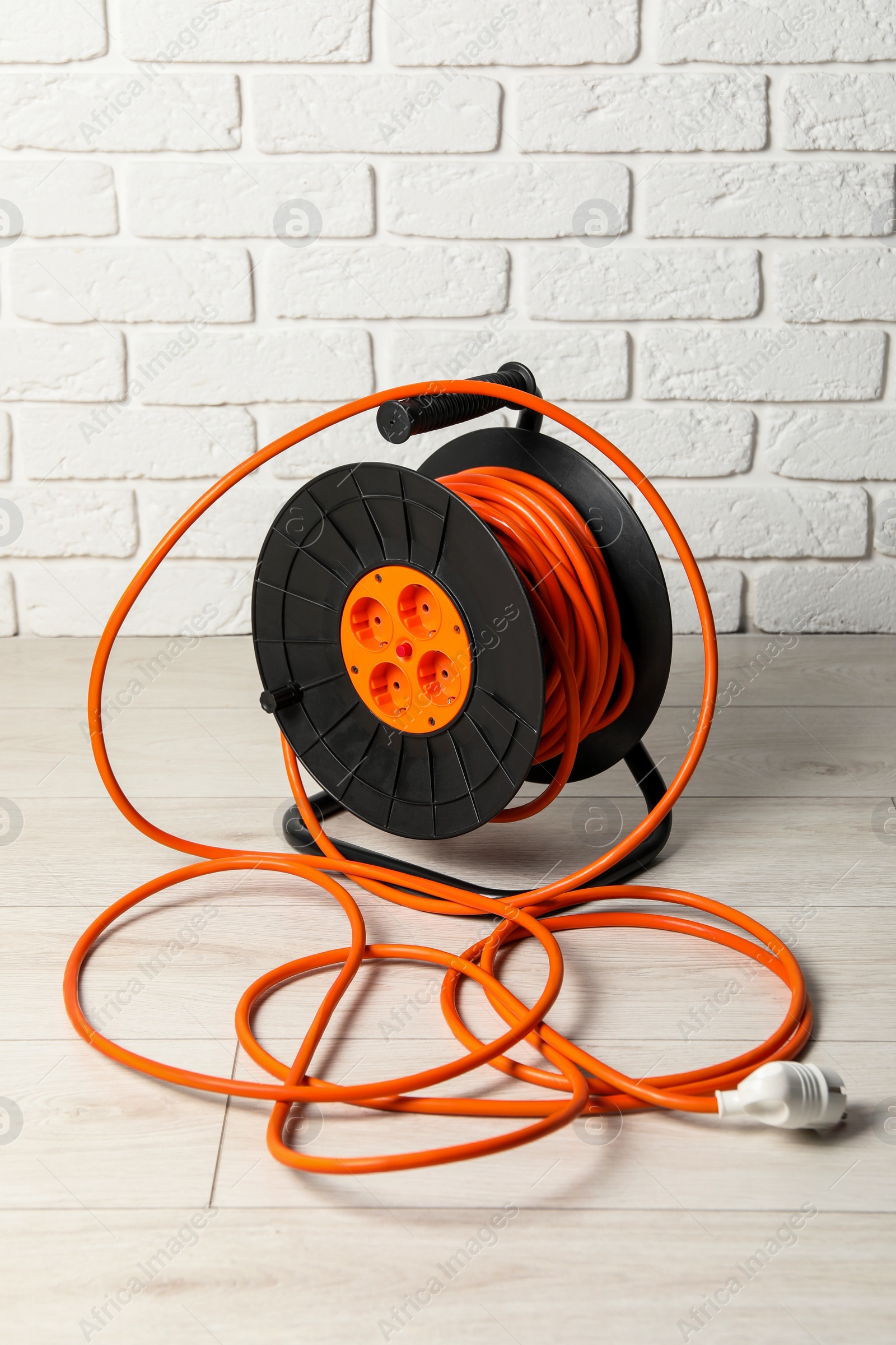 Photo of Extension cord reel on floor near white brick wall. Electrician's equipment