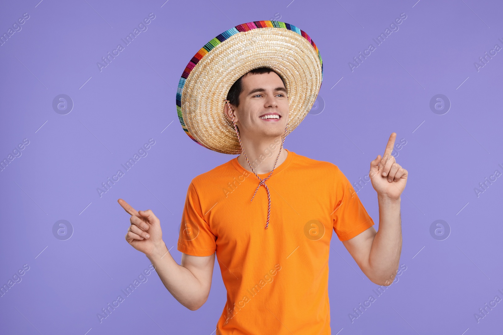 Photo of Young man in Mexican sombrero hat pointing at something on violet background